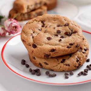 Three chocolate chip cookies on a white plate with a red rim.