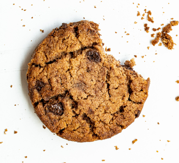 A cookie is sitting on the table with crumbs.